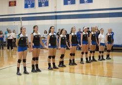 KCC's women's volleyball stands on the court holding hands during the National Anthem before a match.