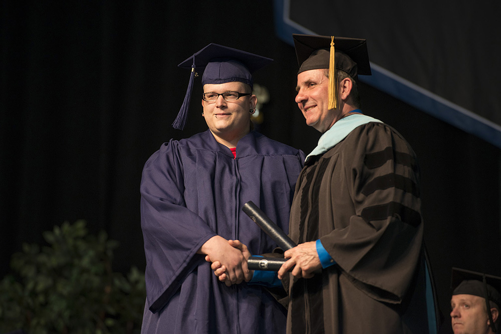 A graduate poses onstage with KCC President Dr. Dennis Bona during the College's 2014 commencement ceremony.