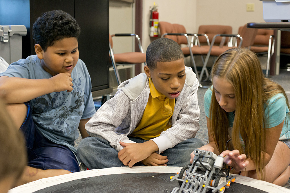 Two young boys and a girl work with a robot during a youth robotics camp at KCC's RMTC.