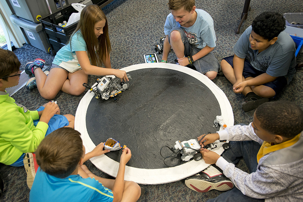 Youth robotics campers prepare robots for a "sumo" battle on a round board during a KCC Robotics Camp at the RMTC.