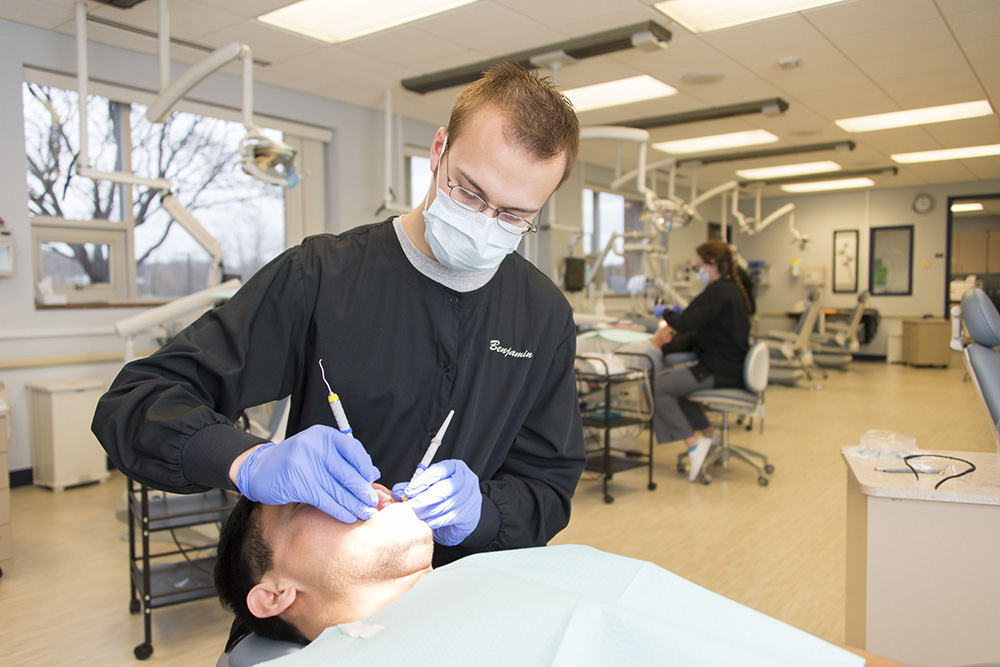 A male Dental Hygiene student cleans the teeth of another student in the college's Dental Hygiene Clinic.