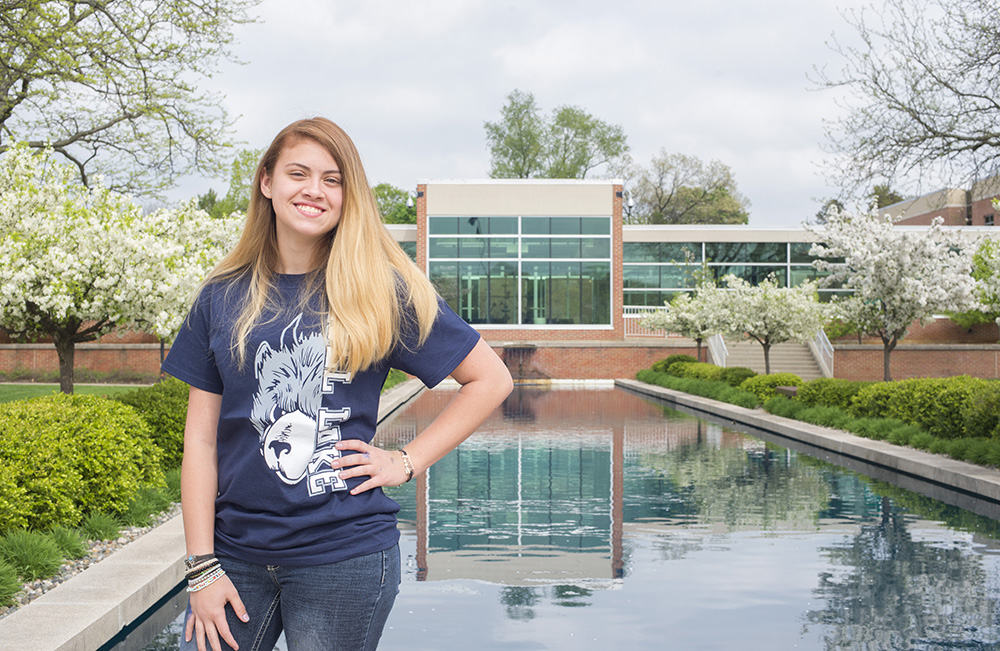 KCC alumna Noel Ramos poses at the main entrance to KCC's North Avenue campus in Battle Creek.