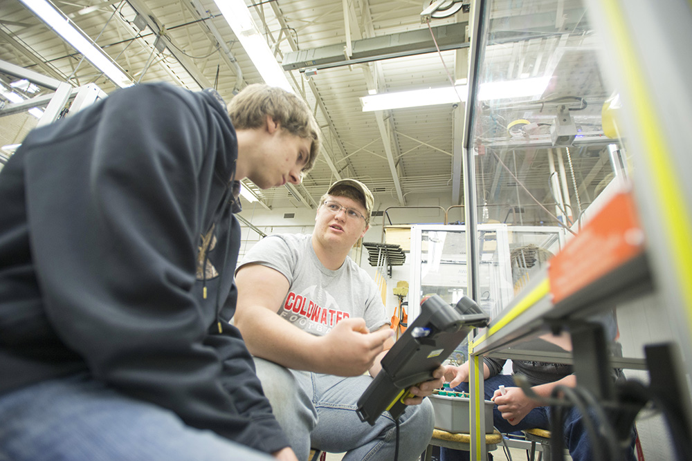 High school senior Kyle Myers holds a tablet-sized controller at the BACC as fellow senior Nick Pierucki points at the screen, giving instructions.