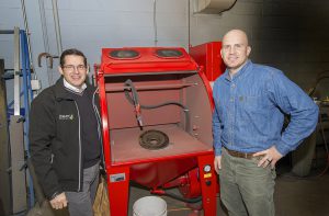 Rosler CEO Bernhard Kerschbaum, left, and KCC Welding instructor Steve Casselman stand in front of a new hand blast finishing cabinet donated by Rosler.