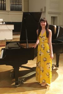 KCC alumnu Abigail Mullis stands next to a piano.