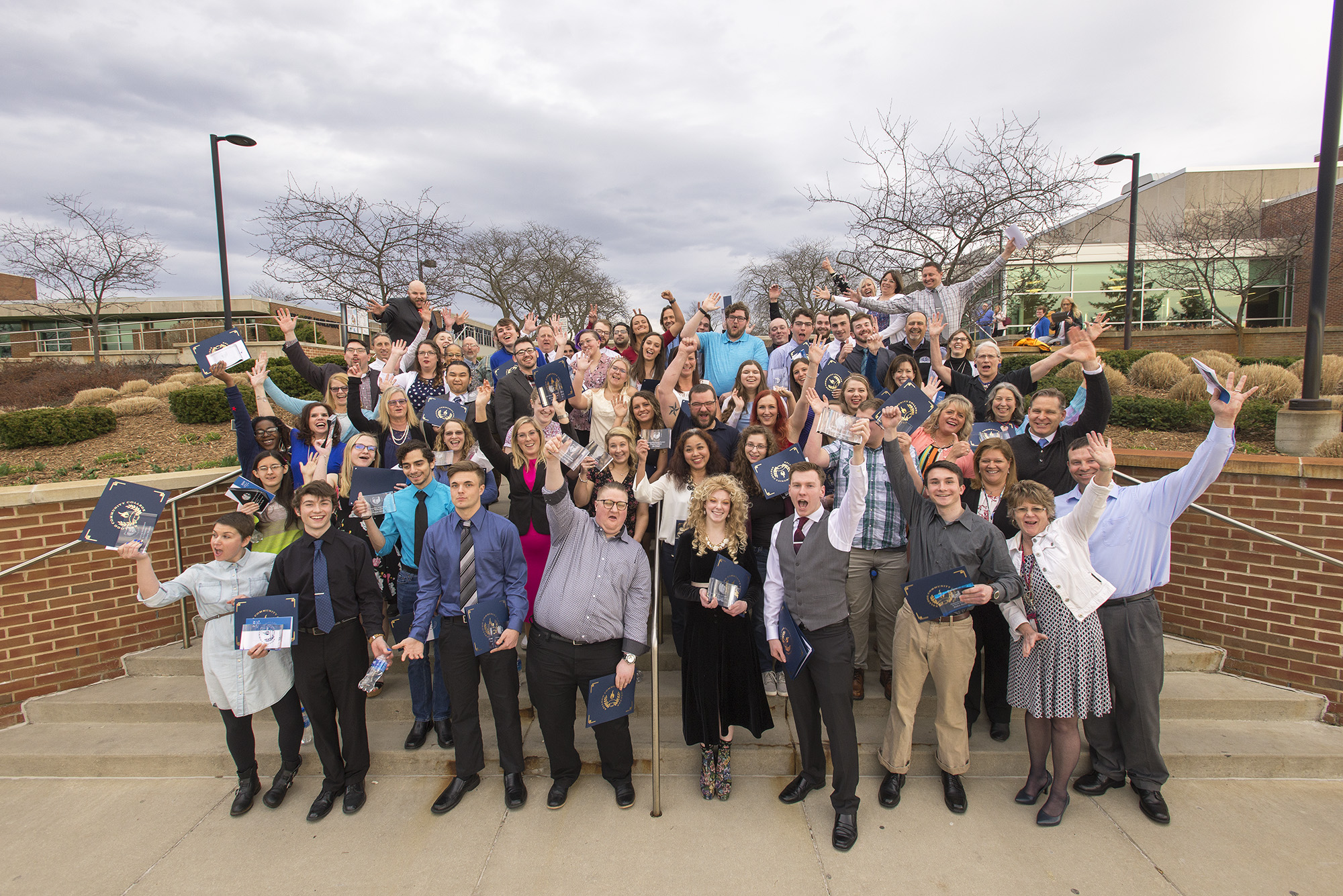 A group photo of KCC's 2019 Outstanding Bruin Award winners and presenters celebrating on the steps at the front of KCC's North Avenue campus in Battle Creek.