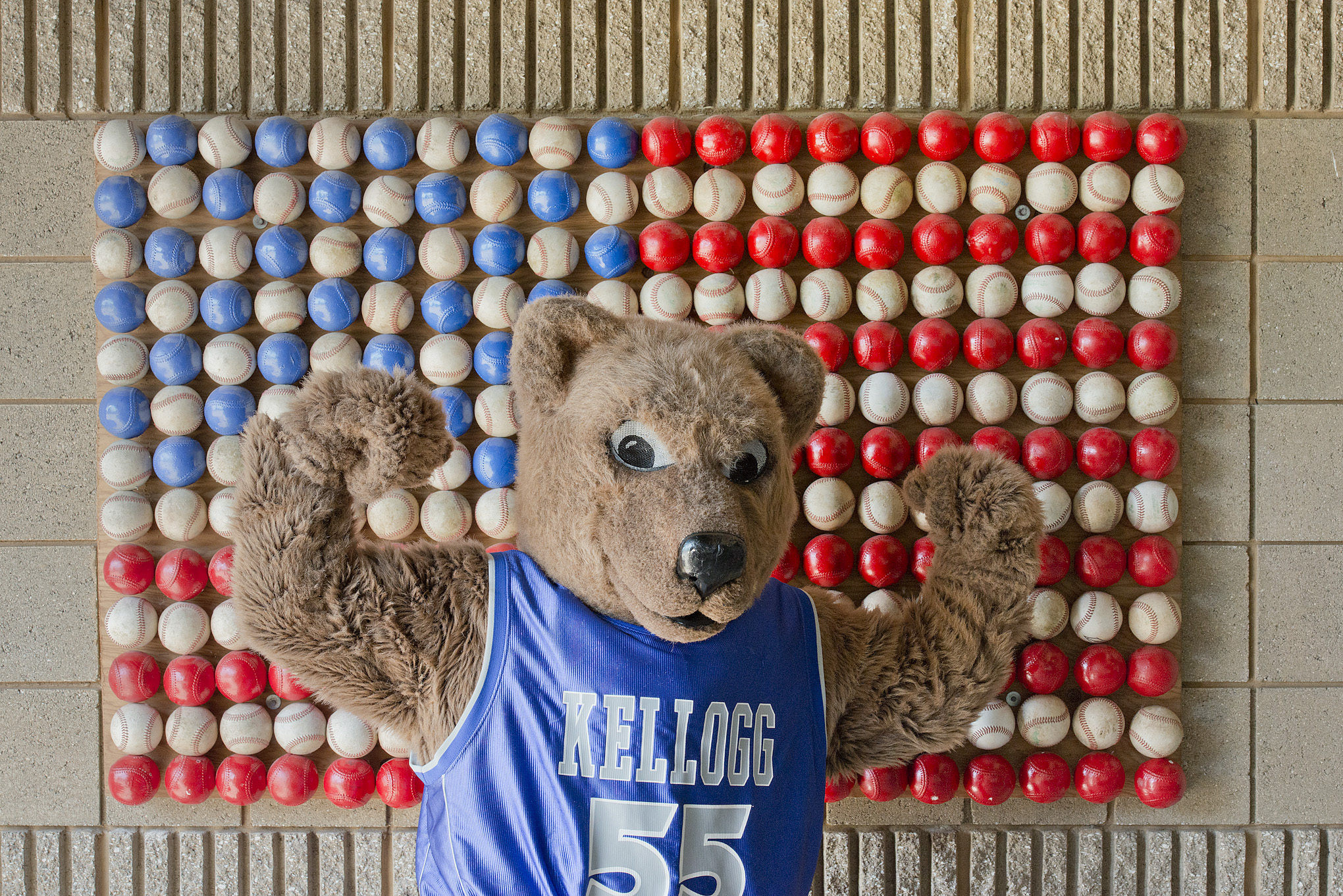 KCC mascot Blaze flexes in front of an American flag made of baseballs at C.O. Brown Stadium.