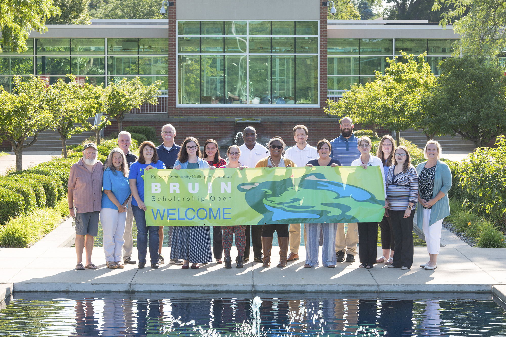 A group photo of KCC staff and Bruin Open volunteers holding a Bruin Scholarship Open banner between the reflecting pools on campus.