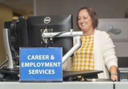 An employee works on a computer behind a sign that reads "Career & Employment Services."