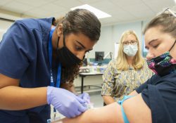 A phlebotomy student draws blood during class.