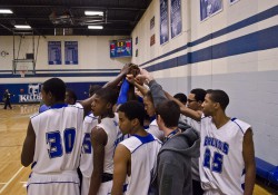 Members of KCC's men's basketball team join hands in a huddle during a game at the Miller Gym