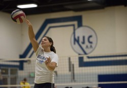 A KCC women's volleyball player hitting a volleyball in the gym.