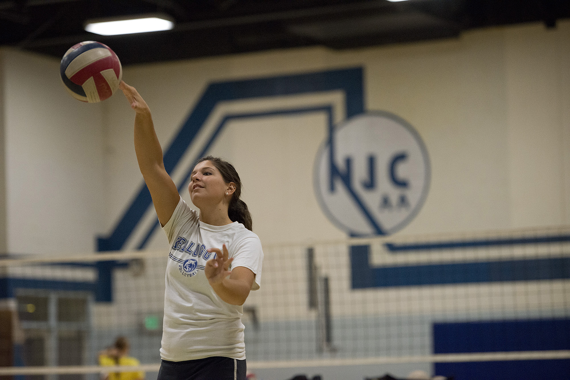 A KCC women's volleyball player hitting a volleyball in the gym.