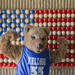 Blaze, KCC's mascot, flexes in front of an American flag made of baseballs at C.O. Brown Stadium