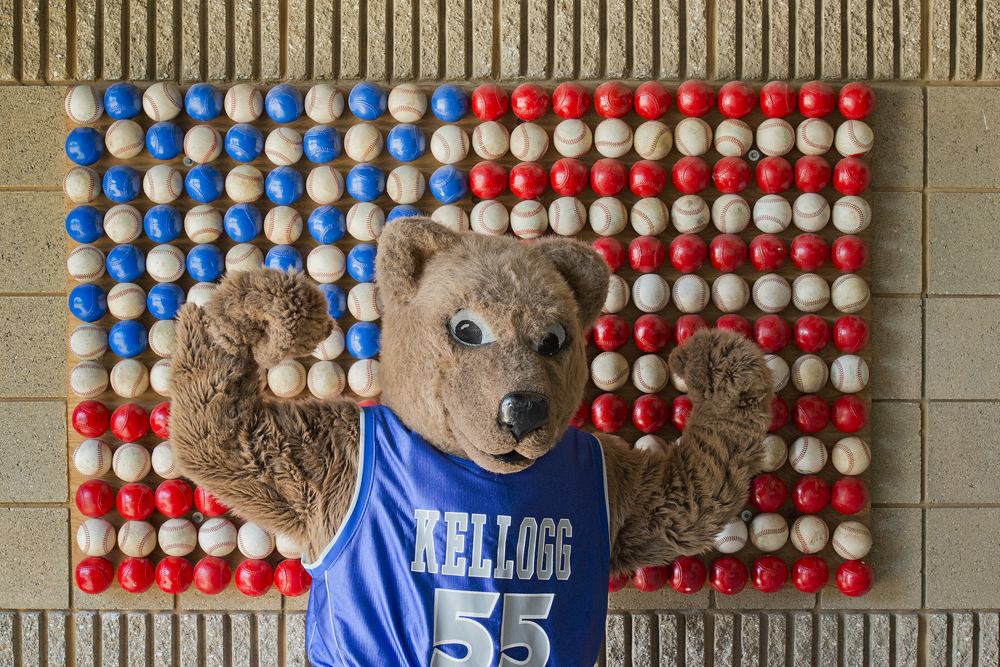 Blaze, KCC's mascot, flexes in front of an American flag made of baseballs at C.O. Brown Stadium