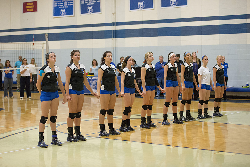 KCC's women's volleyball stands on the court holding hands during the National Anthem before a match.