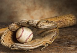 A baseball in a baseball glove, lying beside a baseball bat.