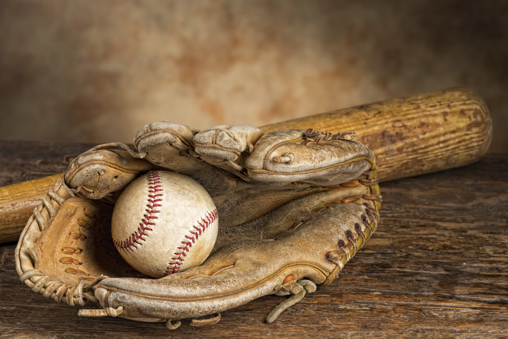 A baseball in a baseball glove, lying beside a baseball bat.