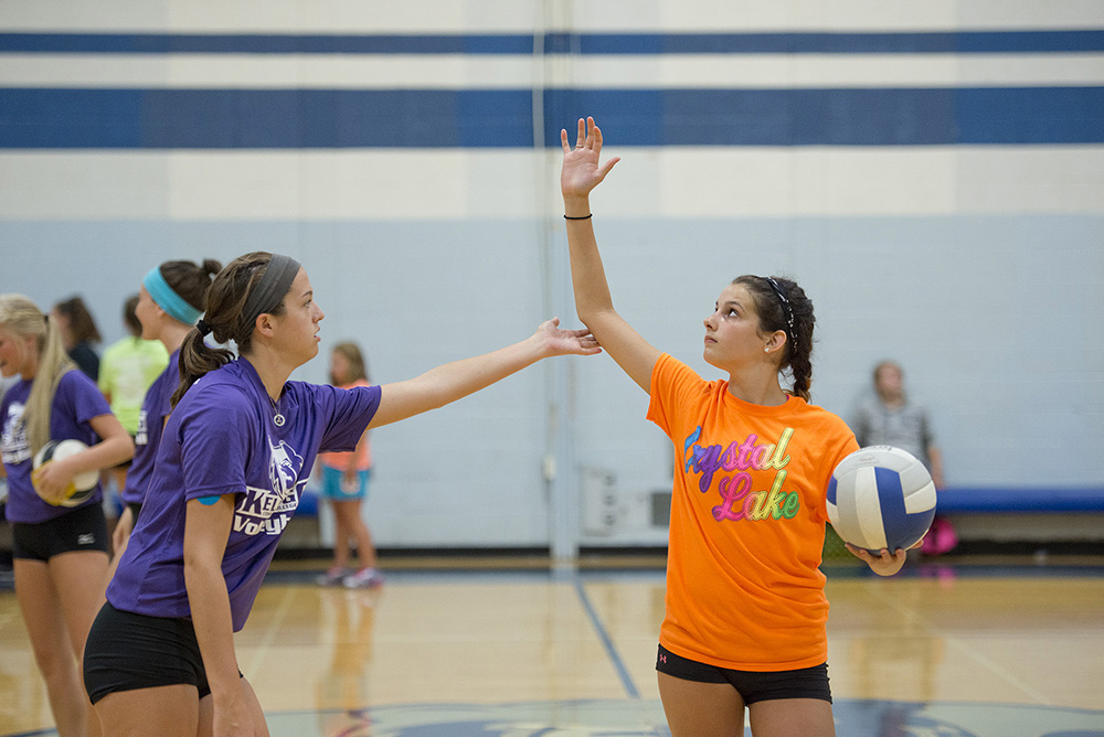 A KCC women's volleyball player assists a youth camp participant in the Miller Gym.