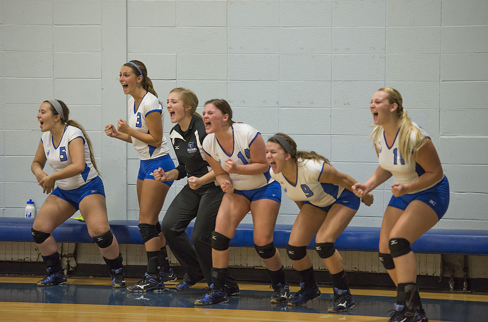 KCC volleyball players express excitement on the bench after a point is scored during a home match.