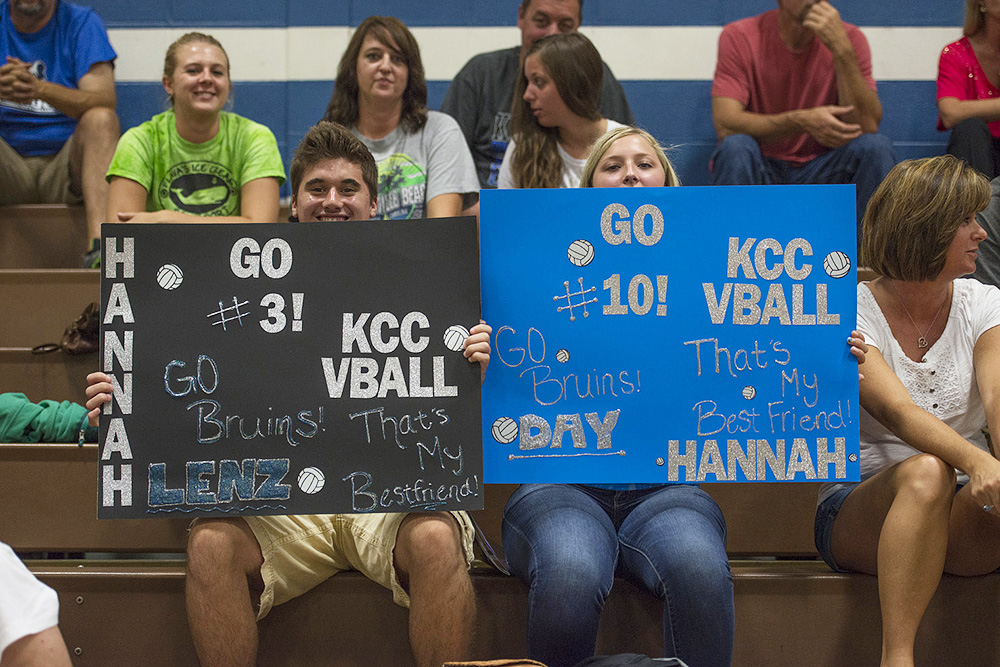 Volleyball team supporters hold signs during a home match.