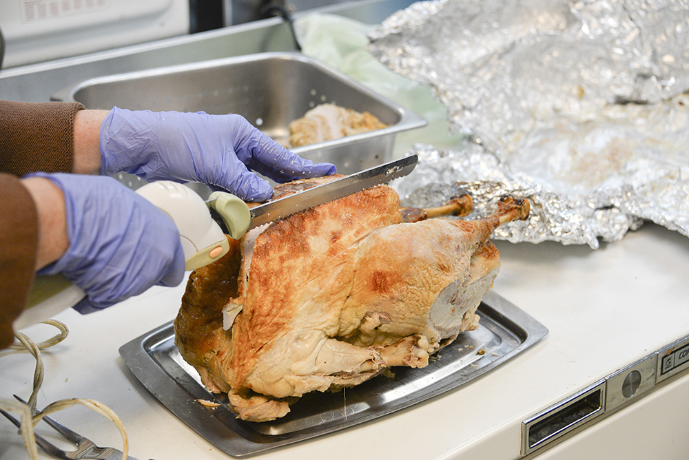 A person's hands are show carving a cooked turkey with an electric knife.