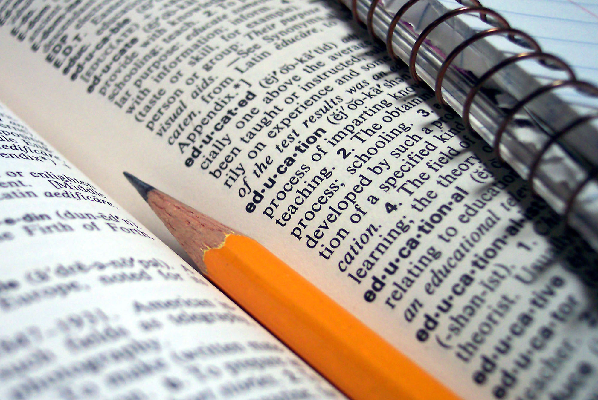 Stock photo of a pencil and notebook laying in a dictionary opened to the entry on education.