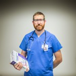 A male nursing student poses, standing with a textbook, in a nursing lab