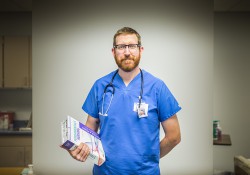 A male nursing student poses, standing with a textbook, in a nursing lab
