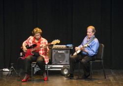 A female music student performs onstage with a guitar with instructor Paul Freeburn, also on guitar.