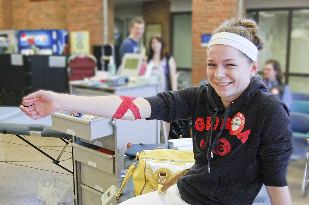 A smiling female student holds up her right arm to show the bandage over the place she gave blood during a blood drive in the Student Center.