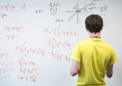 A student faces a white board to work on a math problem.