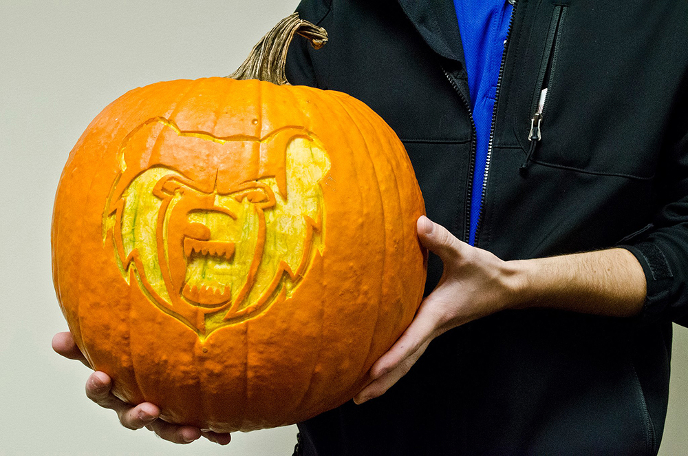 A student holds a pumpkin with a design of the KCC mascot Blaze carved into it.