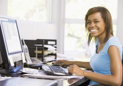 A woman sits in front of a computer, smiling.