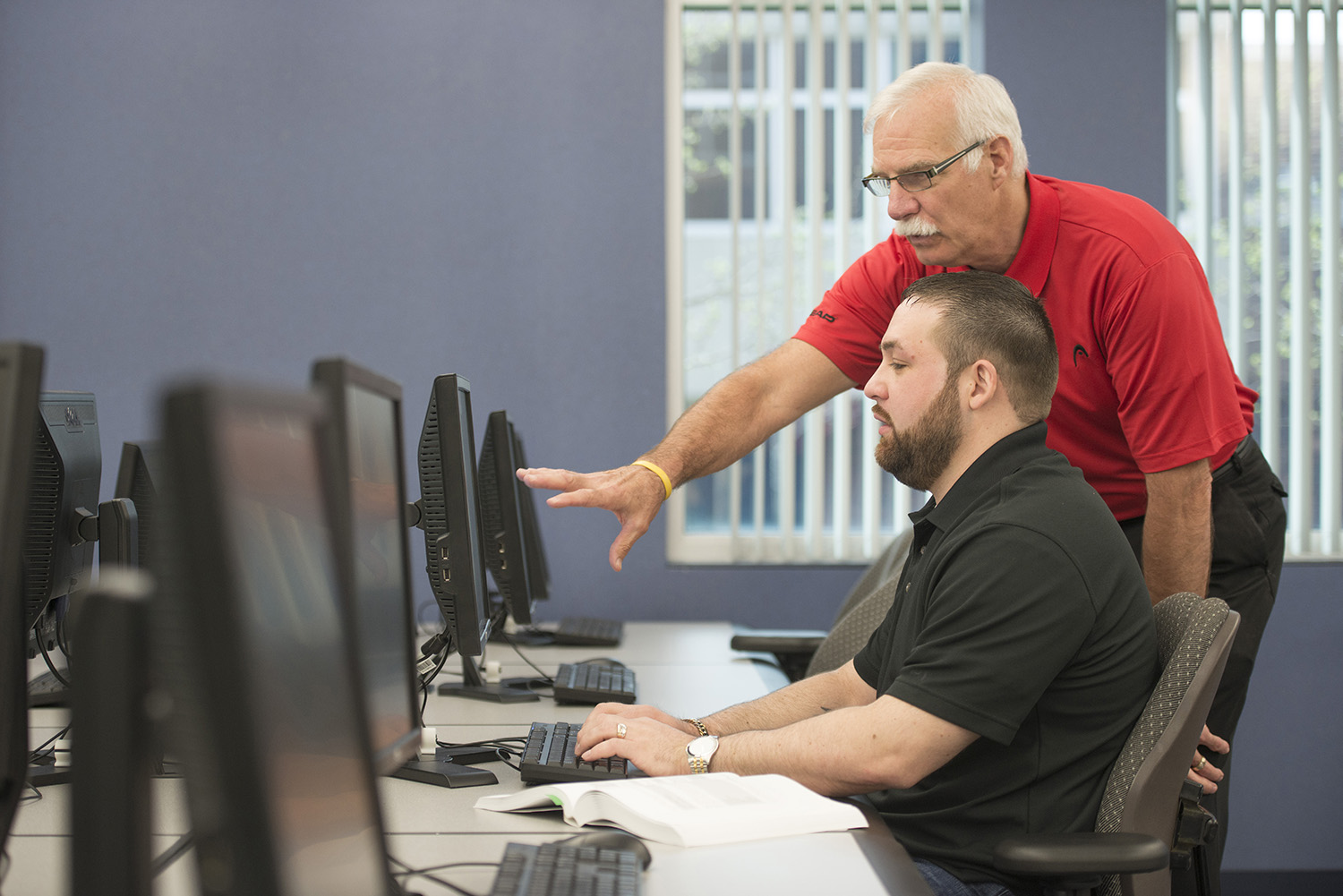 An instructor helps a student in a computer lab.