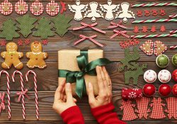 Stock photo featuring female hands over Christmas gifts and homemade gingerbread cookie with handmade decoration on a wooden background.