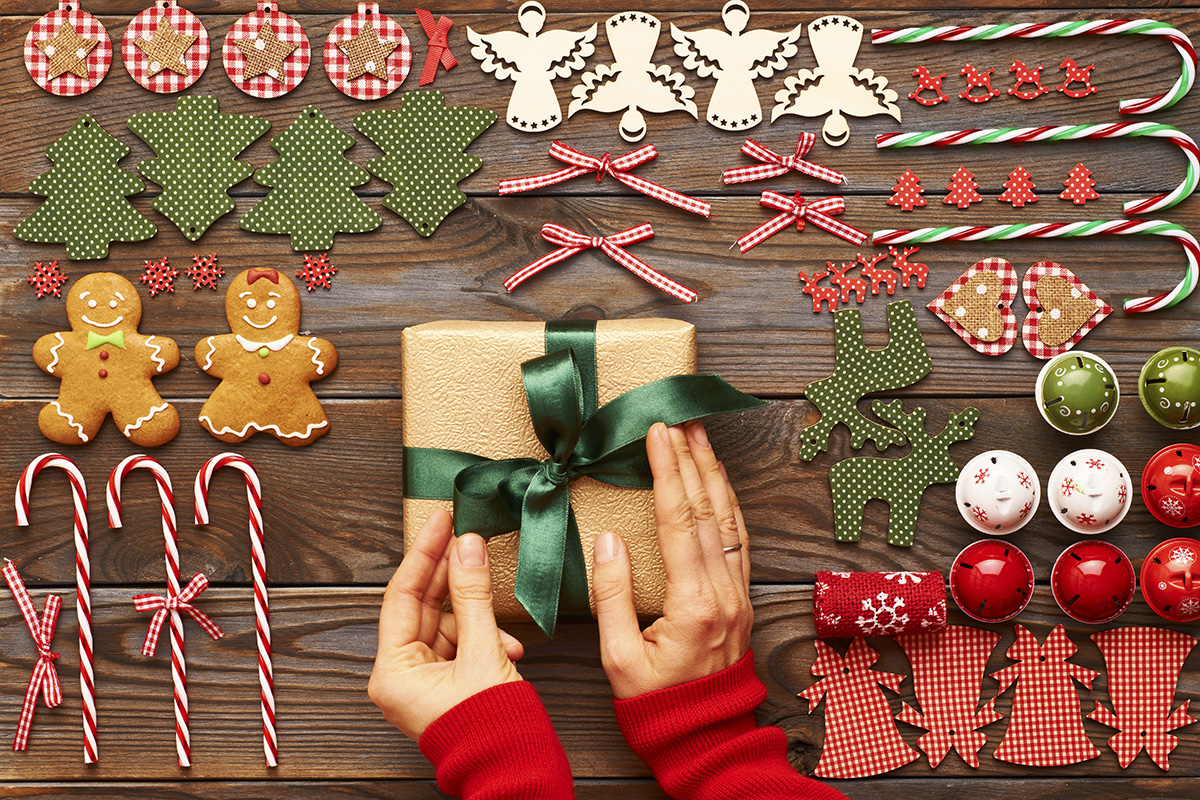 Stock photo featuring female hands over Christmas gifts and homemade gingerbread cookie with handmade decoration on a wooden background.