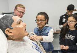 Lakeview Middle School student Van Tling checks the heartbeat of a patient simulator at Kellogg Community College while classmate Sarah Cha and Western Michigan University Homer Stryker M.D. School of Medicine student Zackary Cowan observe.