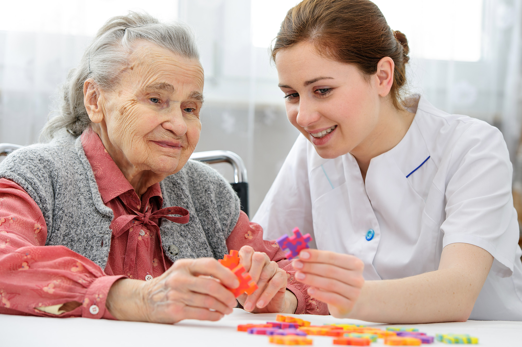 Stock photo of an elder care nurse playing a jigsaw puzzle with a senior woman in a nursing home.