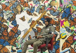 Artist Jaziel Pugh sits in front of his mural "Six Disciplines."