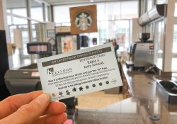A hand holds a free-coffee card in the foreground with KCC's Mini Cafe in the background.