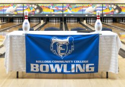A table in a bowling alley covered with a cloth featuring the KCC logo and the words "Kellogg Community College Bowling."