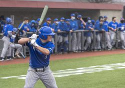 A KCC baseball player bats while the team watches from the dugout.
