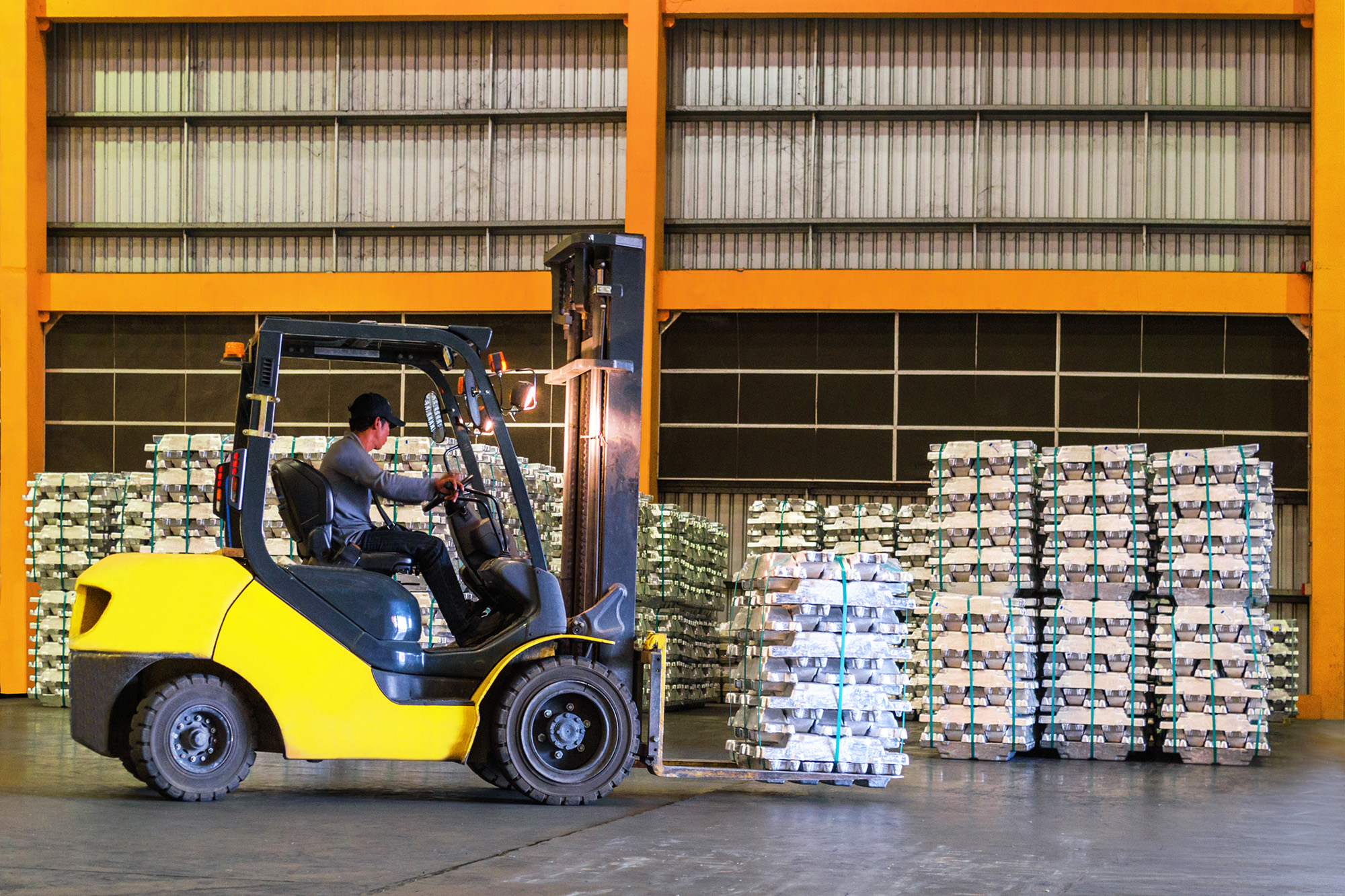 A man lifts a pallet stacked with bags using a forklift.