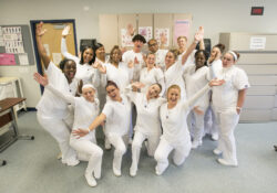 A group photo of CNA graduates celebrating their graduation in a CNA Lab on campus.