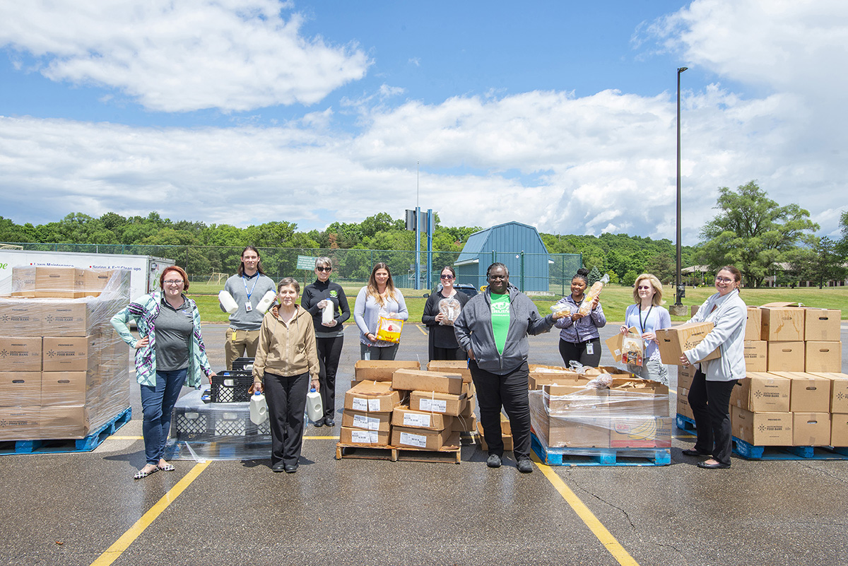 Employees pose with boxes of food for donation outside.