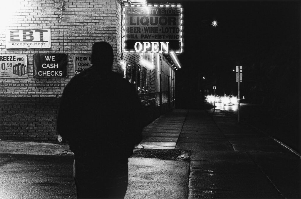 Black and white photo showing the silhouette of a man walking in a city at night.