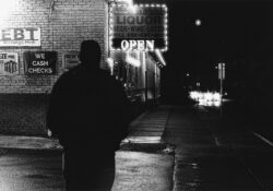 Black and white photo showing the silhouette of a man walking in a city at night.