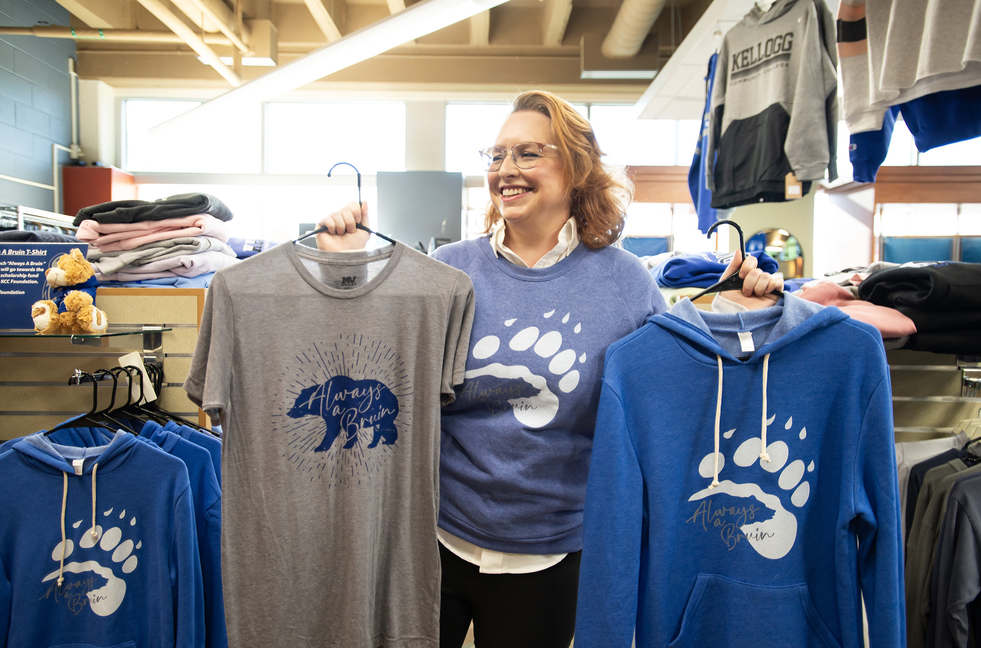 A KCC employee holds up Always a Bruin shirts in the bookstore.