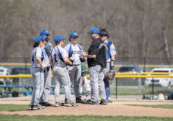 Coach Laskovy meets with players on the pitcher's mound during a game.